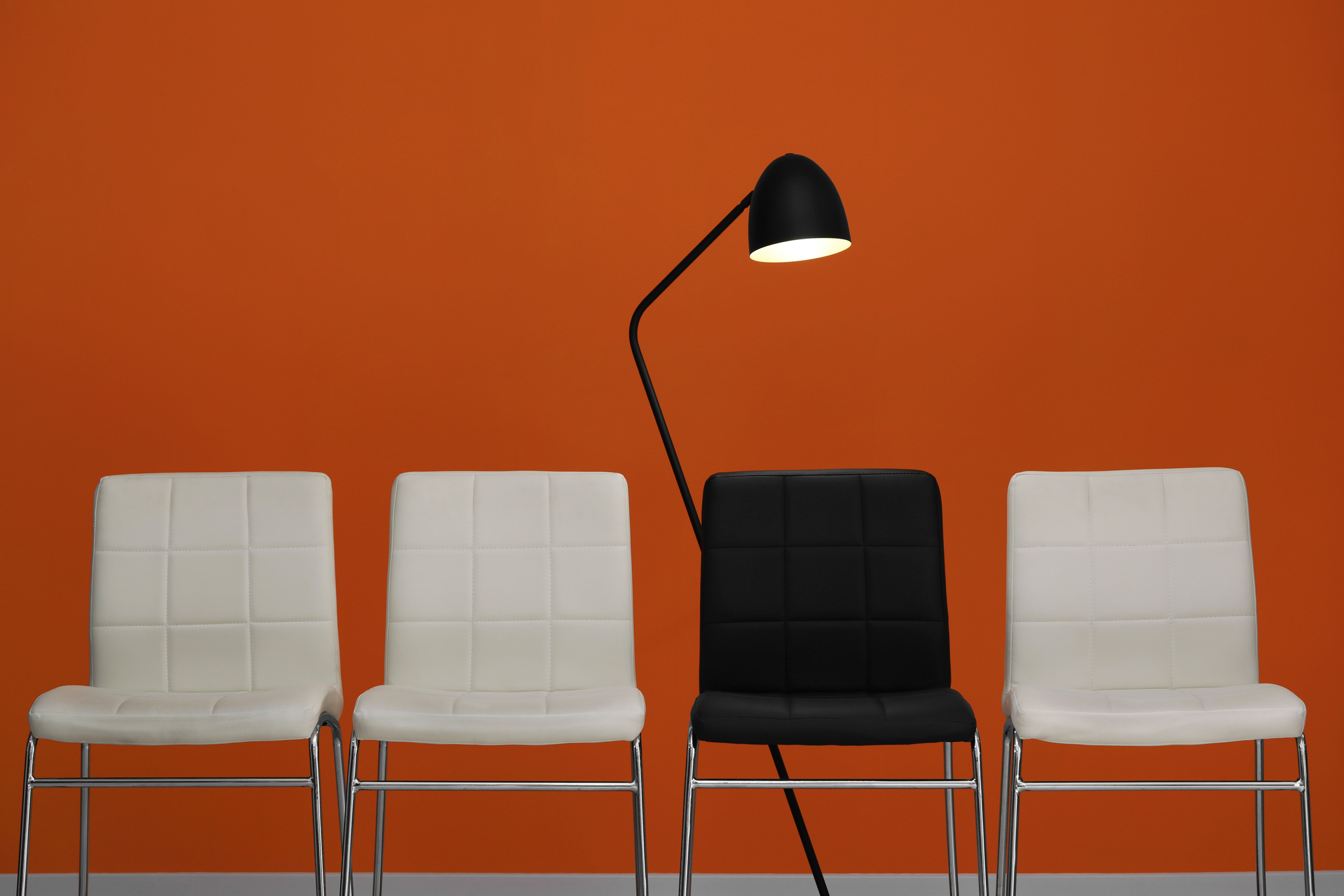 White Chairs with Black One and Lamp near Orange Wall. Recruiter